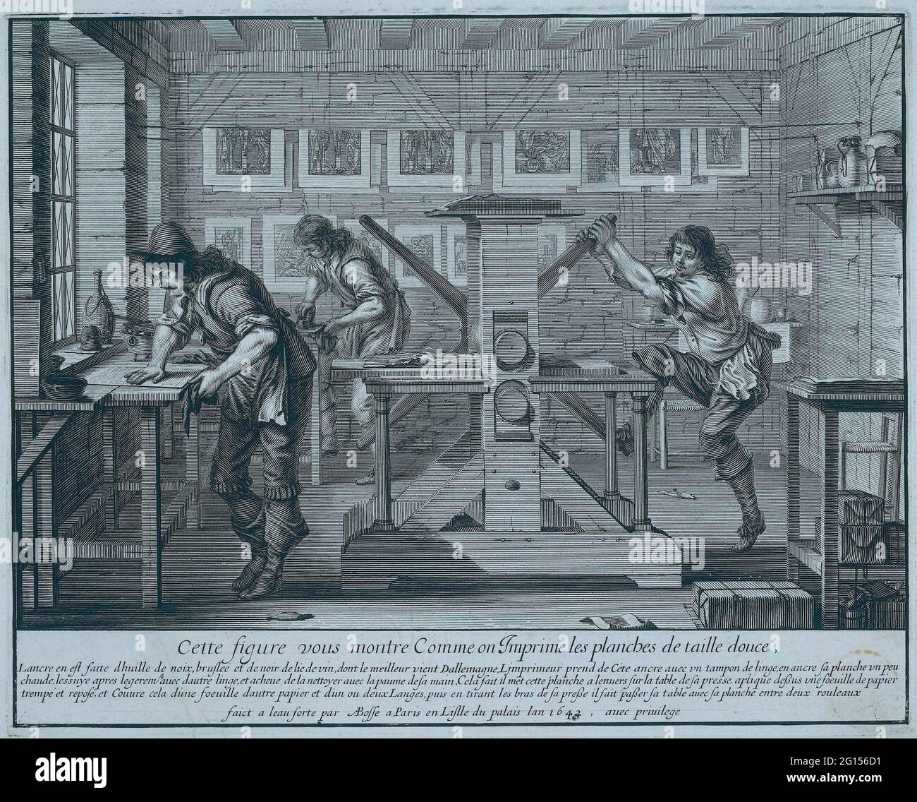PRINT PRESSURE. Pressing etching is demonstrated in the workshop. The printer in the background rubs the ink on the plate. The man for the workbench 'sinks the plate' with the palm of his hand. The clean album, on which the ink is now only in the fine grooves, is printed on the etching press. Stock Photo