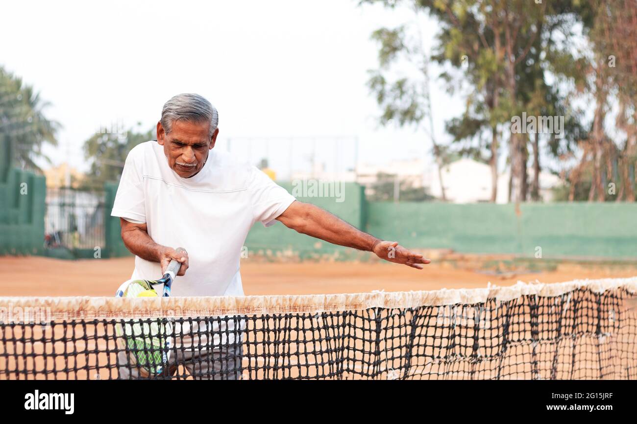 Elderly man practicing tennis near net - Concept of healthy and fit active old people. Stock Photo