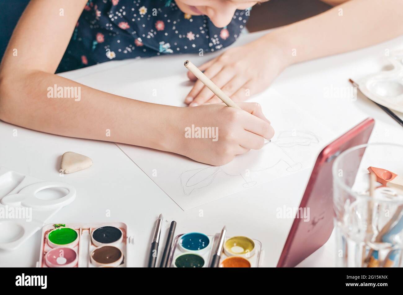 The hands of a cute caucasian girl are drawing a pencil sketch. A girl is watching an online lesson on a smartphone. Classes with children at home. Ha Stock Photo