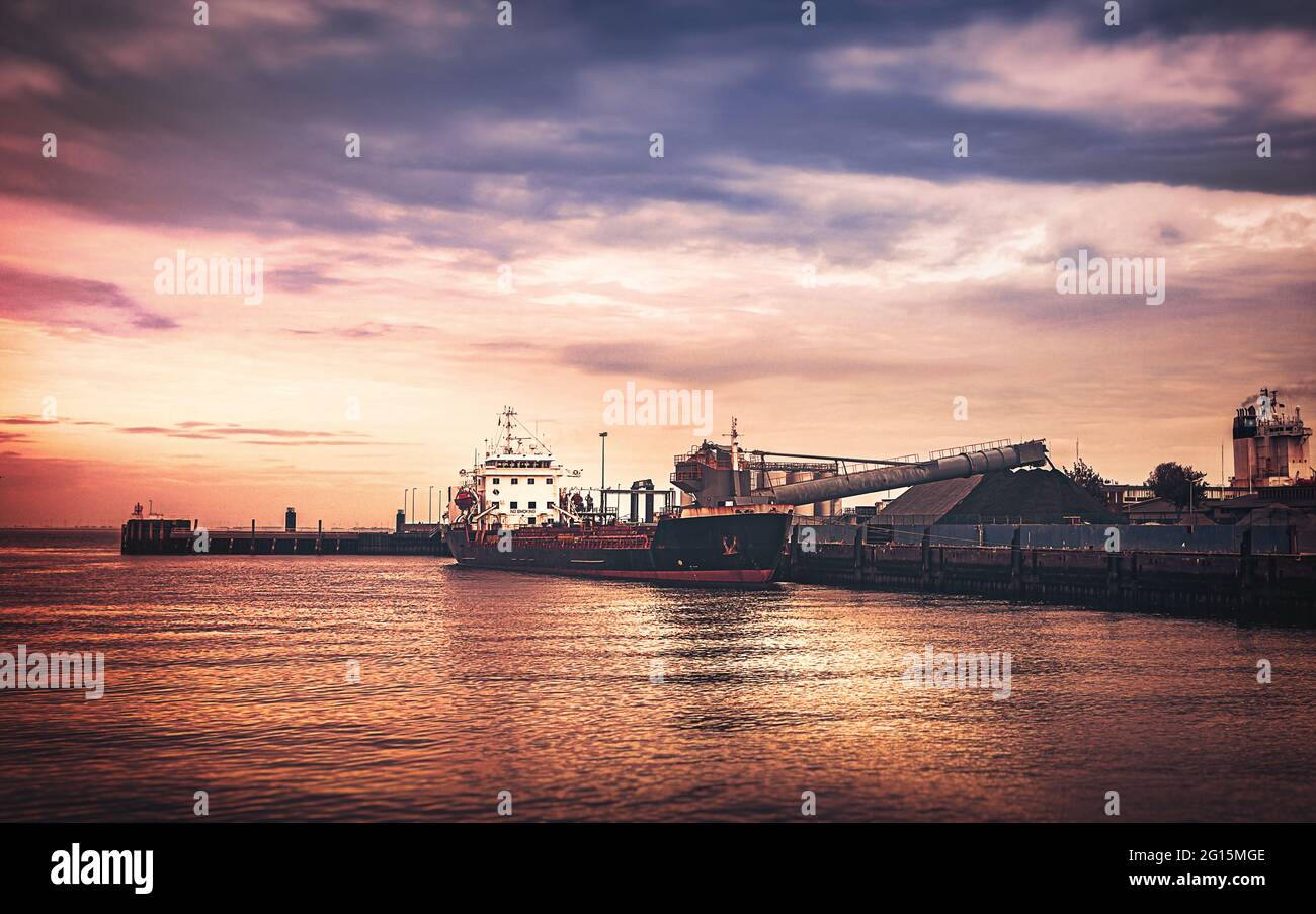 Cuxhafen Containerhafen an der Nordsee mit großem Tanker und Schiffscontainer bei spektakulärer Aussicht und dramatischem Himmel und Wolkenband. Stock Photo