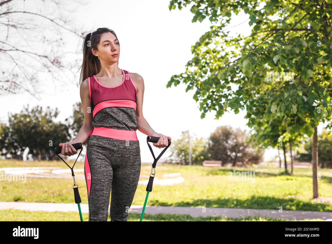 horizontal portrait of a young caucasian woman exercising in a park. She is wearing sport clothes and uses resistance bands Stock Photo