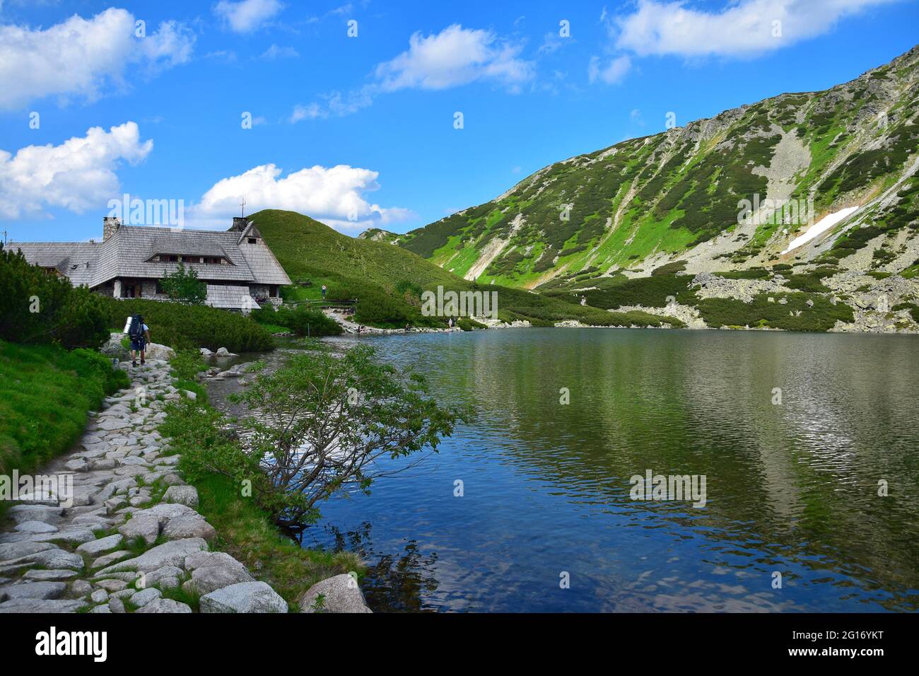 The beautiful lake Przedni Staw and the mountain lodge Schronisko Piec Stawow in the High Tatras, Poland. A trail with a hiker on the left. Stock Photo