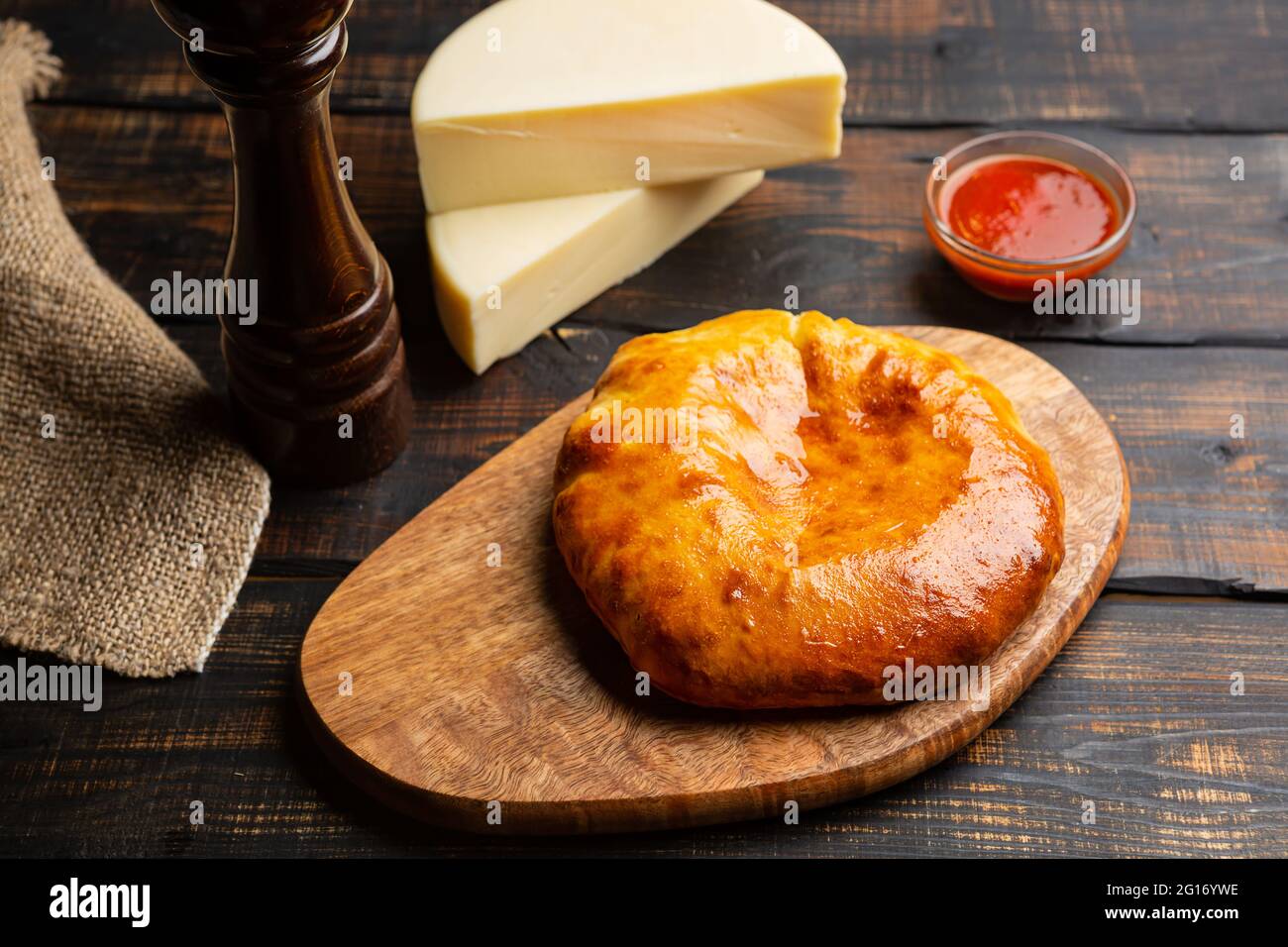 Uzbek khachapuri with cheese with tomato sauce on cutting board on wooden table Stock Photo
