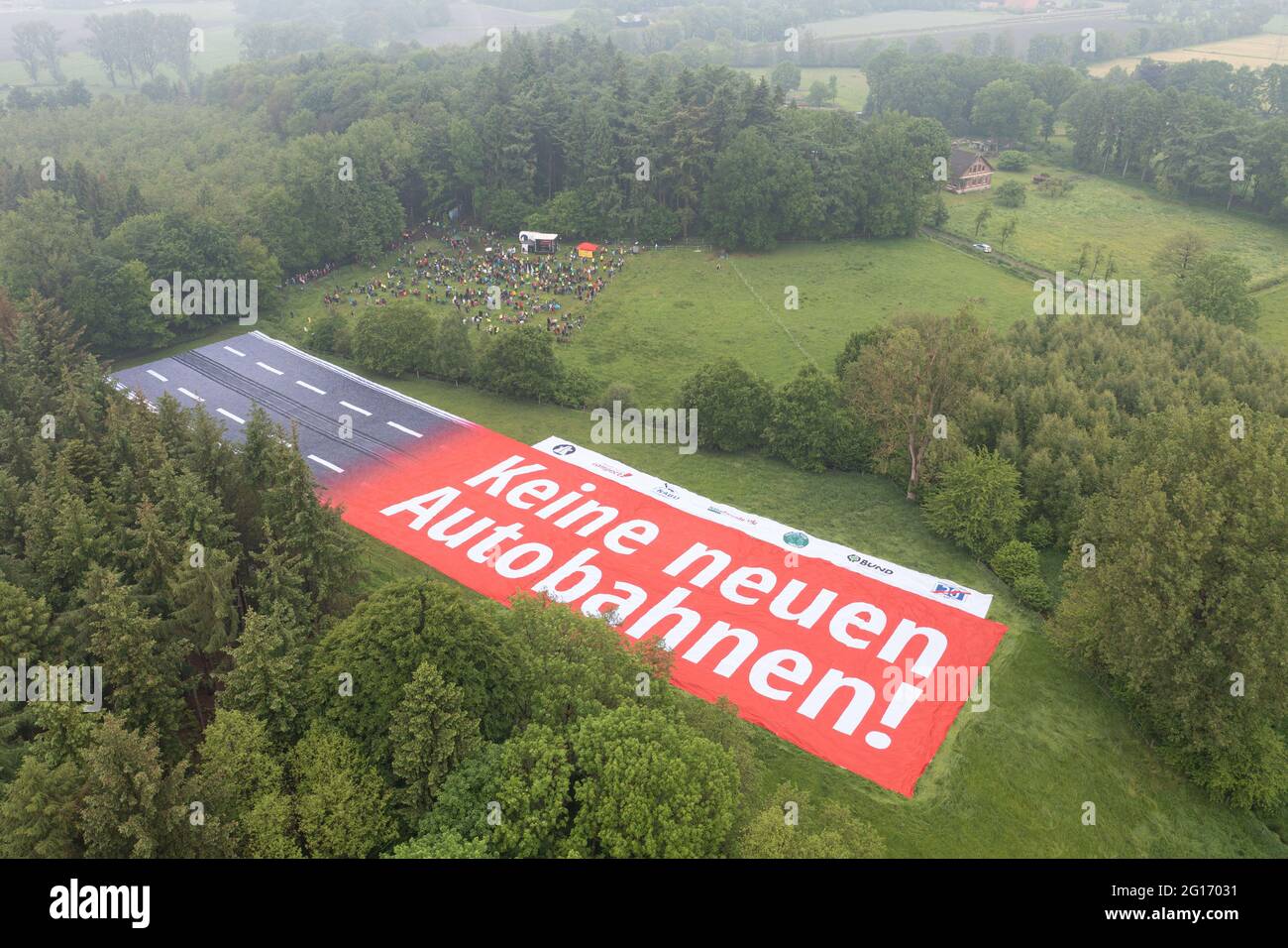 Rastede, Germany. 05th June, 2021. A banner with the inscription 'No new motorways!' representing a section of motorway can be seen on a land area between a forest and a meadow. A protest against the planned construction of the A20 is taking place, in which numerous people are participating (shot with a drone). Credit: Mohssen Assanimoghaddam/dpa/Alamy Live News Stock Photo