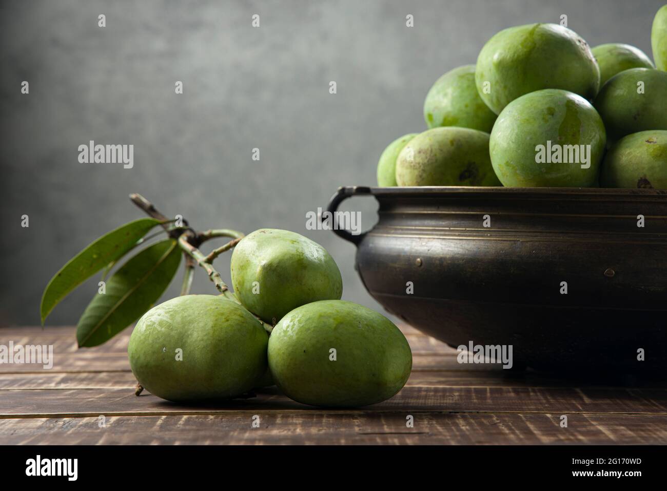Raw Mango arranged traditionally in a brass vessel and bunch of green ...