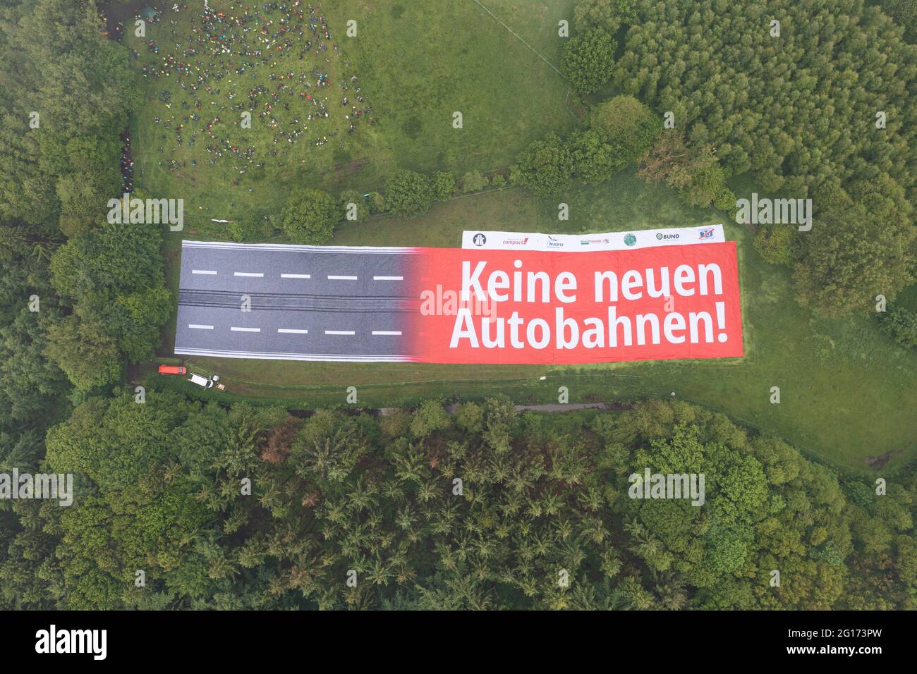 Rastede, Germany. 05th June, 2021. A banner with the inscription 'No new motorways!' representing a section of motorway can be seen on a land area between a forest and a meadow. A protest against the planned construction of the A20 is taking place, with numerous demonstrators taking part (shot with a drone). Credit: Mohssen Assanimoghaddam/dpa/Alamy Live News Stock Photo