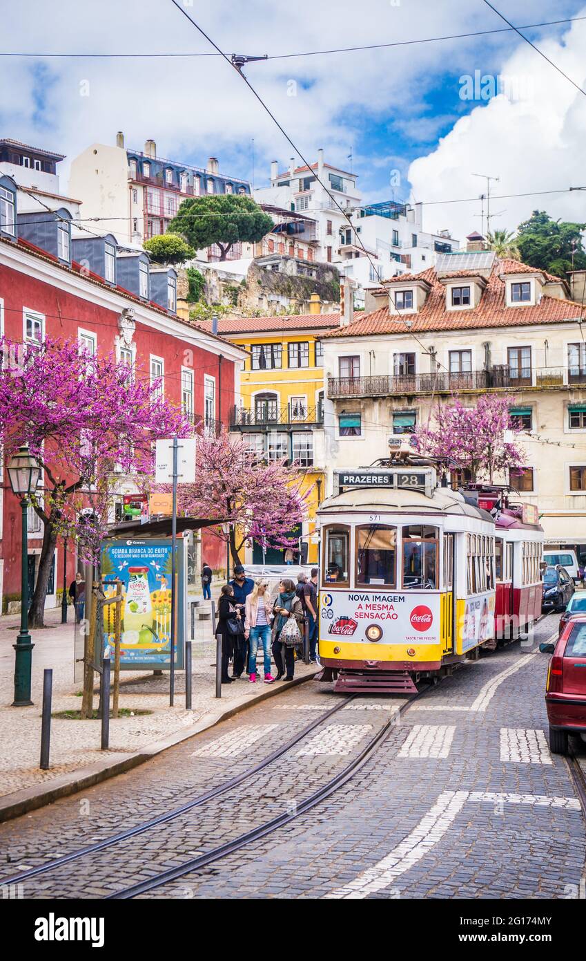 LISBON, PORTUGAL - MARCH 25, 2017: A typical old yellow vintage tram 28 on the street of Lisbon, Portugal. People wait at the tram stop. Stock Photo