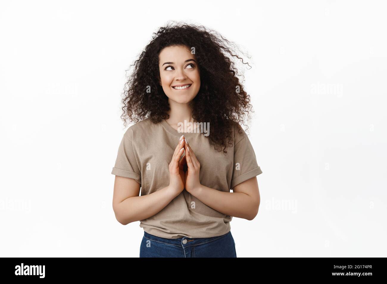 Coy brunette girl scheming, having evil genius idea, steeple fingers and looking devious at upper right corner, smiling thoughtful, standing against Stock Photo