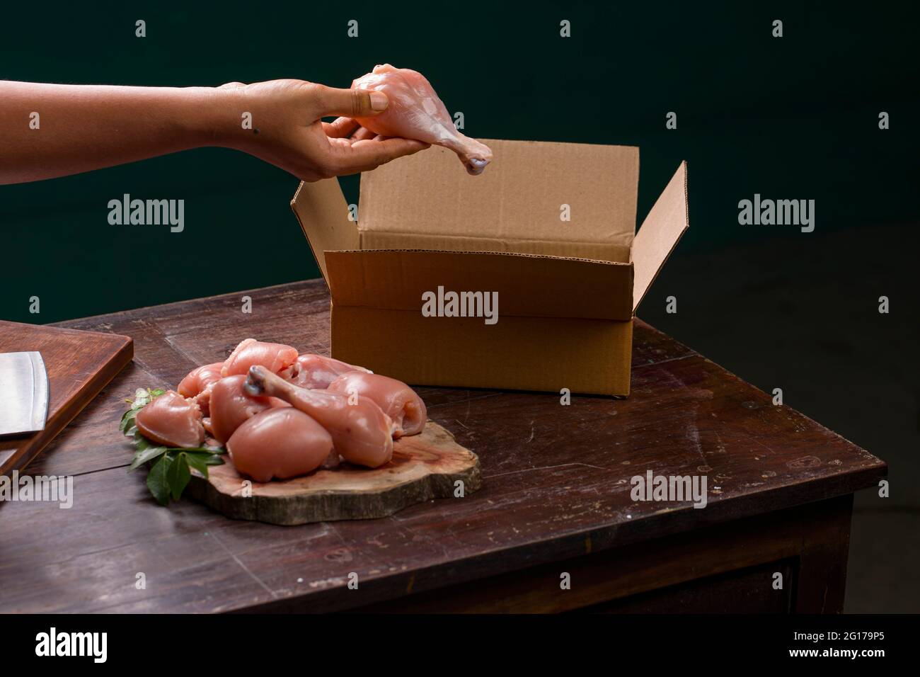 Raw chicken cuts or parts  without skin arranged on a sliced wooden log base and  a worker packing raw chicken for delivery which is placed on wooden Stock Photo