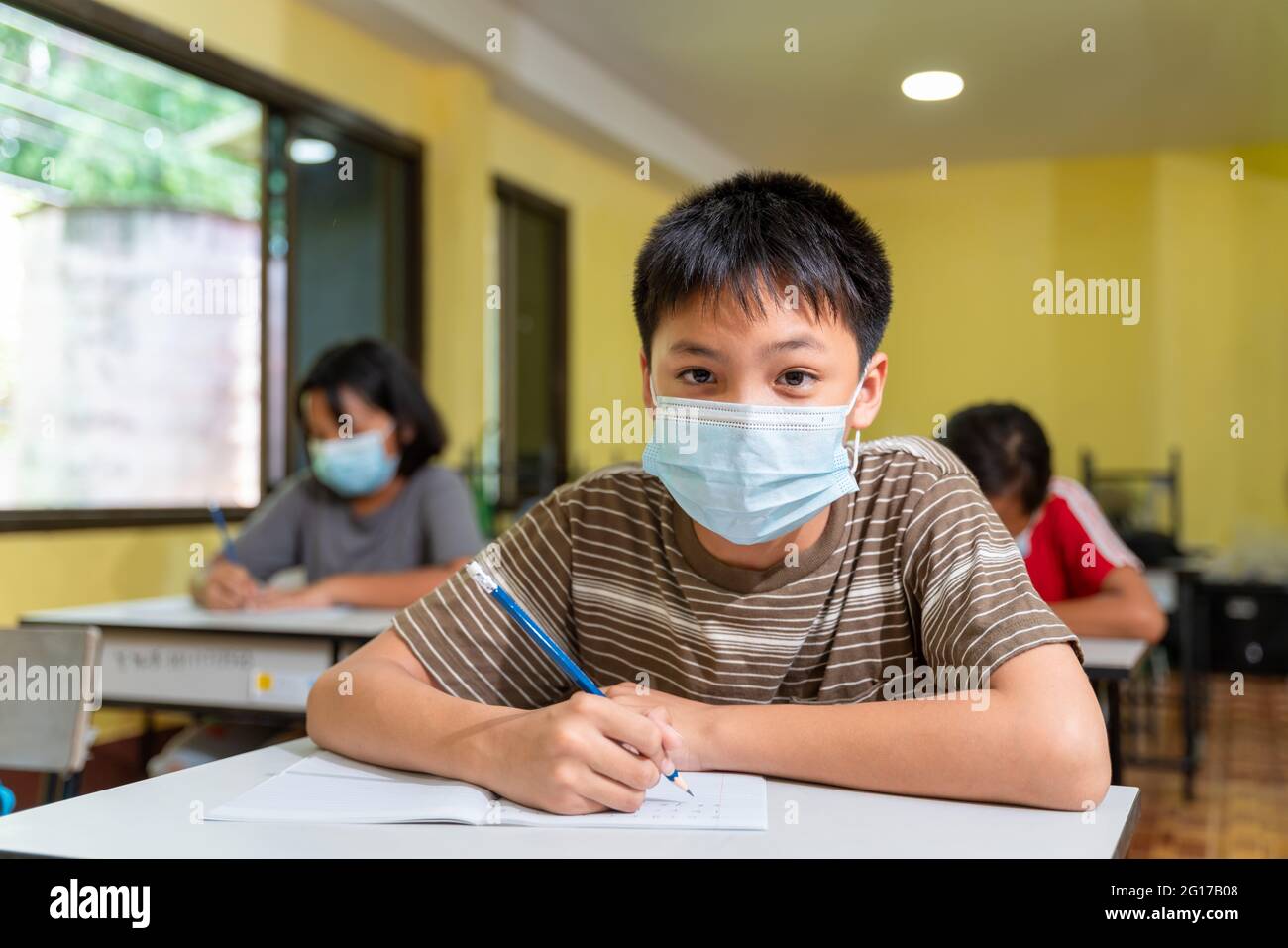 Asian boy in classroom with face mask back at school after covid-19 quarantine and lockdown. Stock Photo