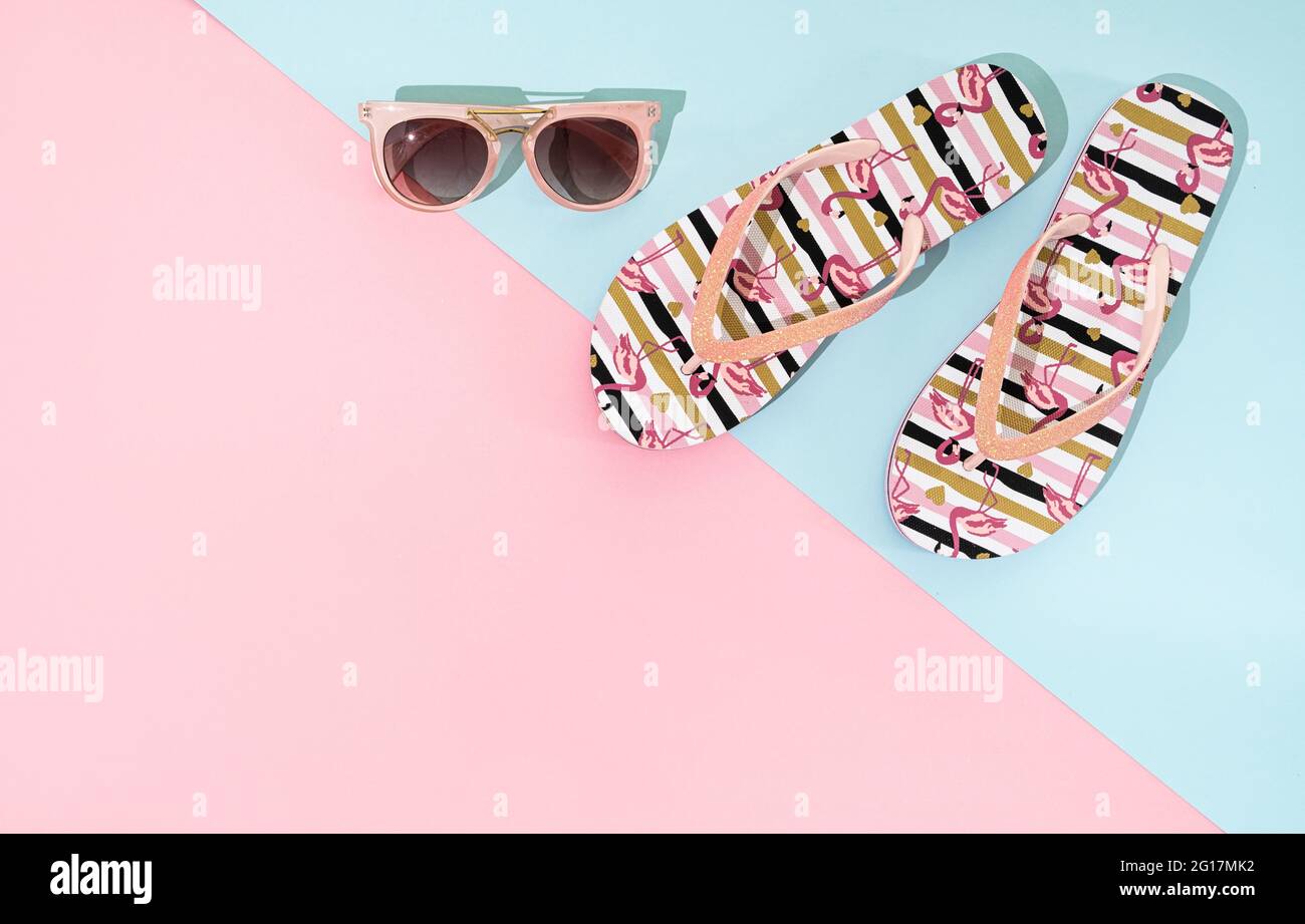 A pair of summer sandals, flip flop and pink sunglasses on pink and blue background, top view, copy space Stock Photo