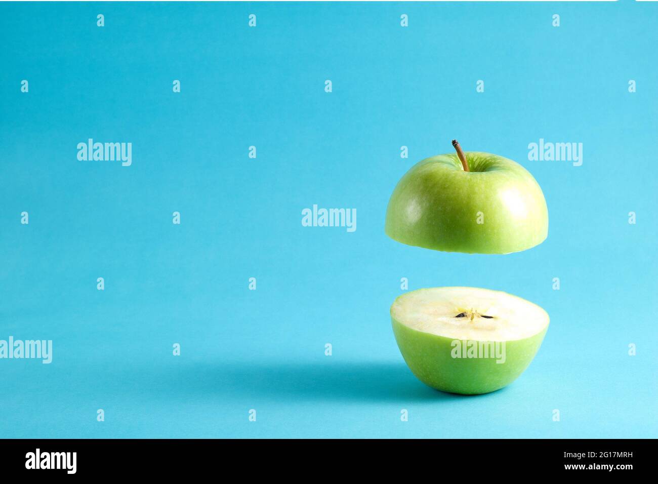 Fresh green apple with a half flying on blue background. Flying green apple with empty copy space for text. Stock Photo