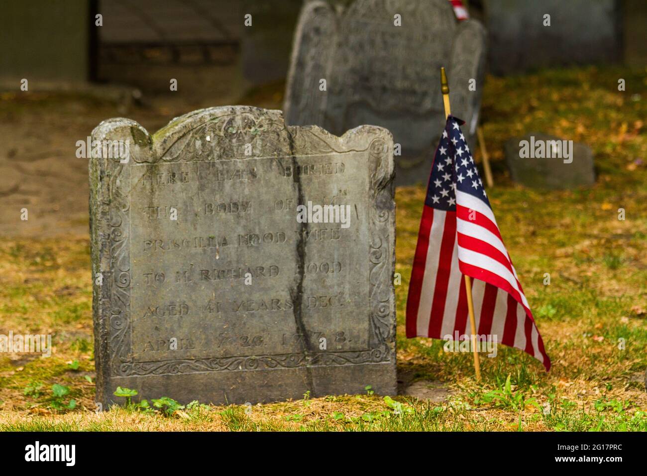 Close up of an ancient grave stone with an American flag next to it at Granary Burying Ground in Boston Stock Photo