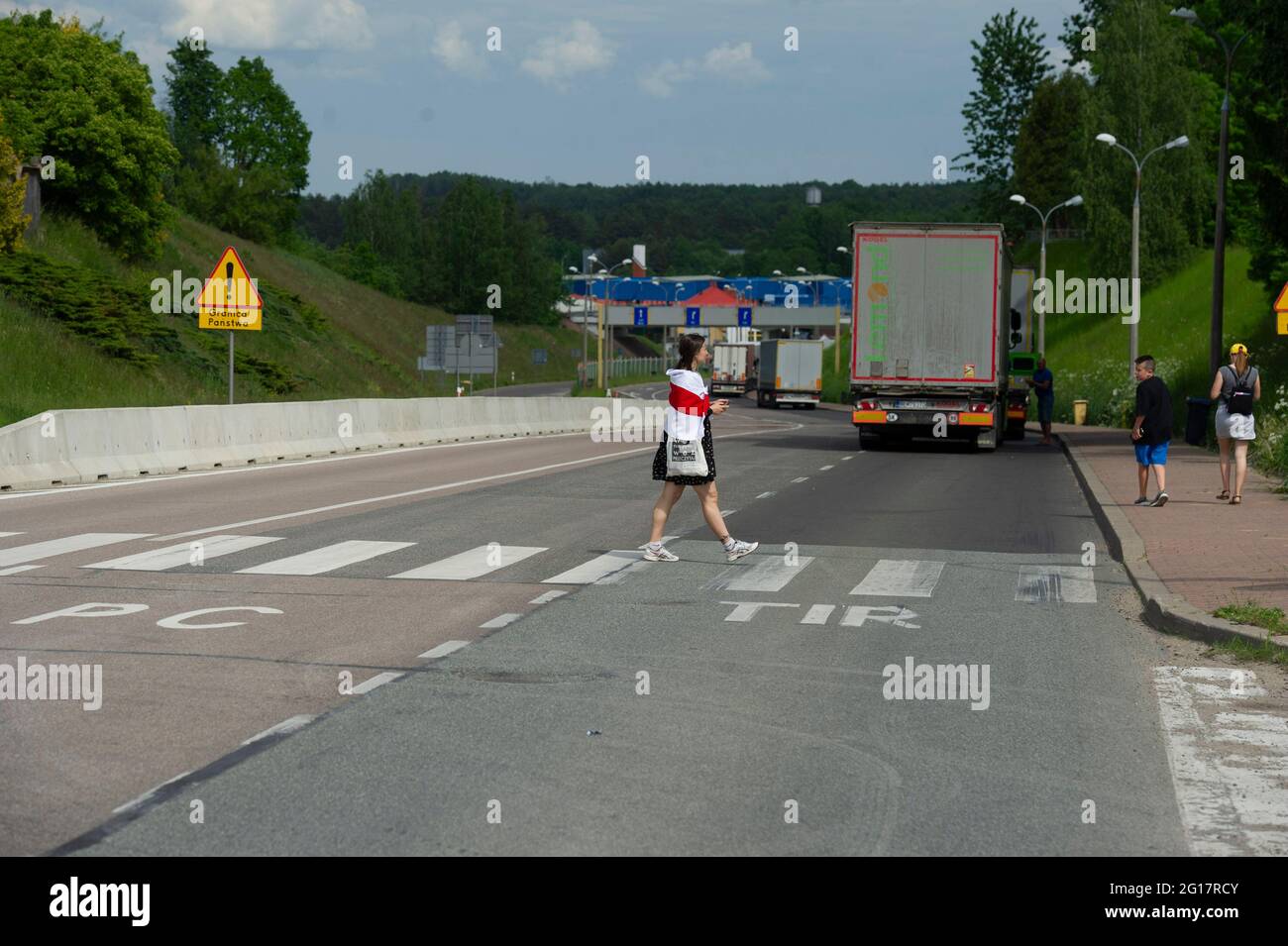Warsaw, Warsaw, Poland. 5th June, 2021. A protester wears a historical Belarusian flag while crossing the street at the Polish-Belarusian border on June 5, 2021 in Bobrowniki, Poland. Around a hundred of Belarusian citizens on exilein Poland gathered in Bobrowniki, on the Polish-Belarusian border to demand sanction from European Union towards the Belarusian government. Credit: Aleksander Kalka/ZUMA Wire/Alamy Live News Stock Photo