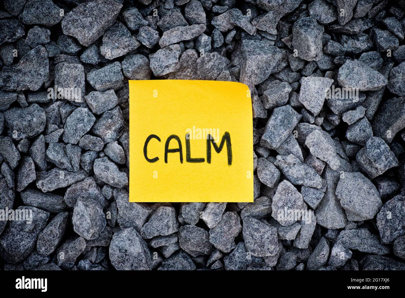 A yellow paper note with 'Calm' written on it lying on a granite background. Close up. Stock Photo