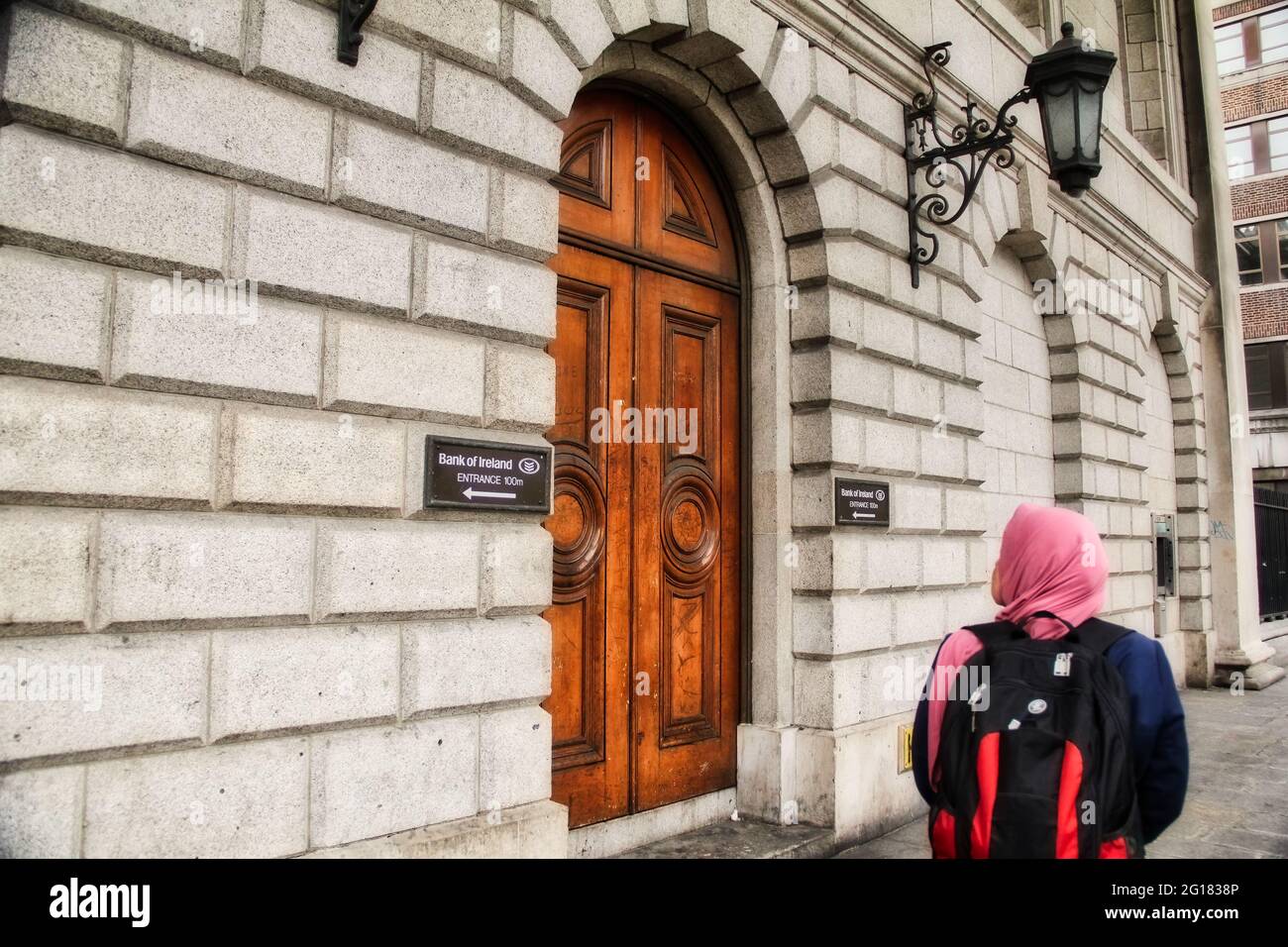 DUBLIN, IRELAND-- MAY 28, 2012: Muslim woman passing by Bank of Ireland wooden door. Stock Photo