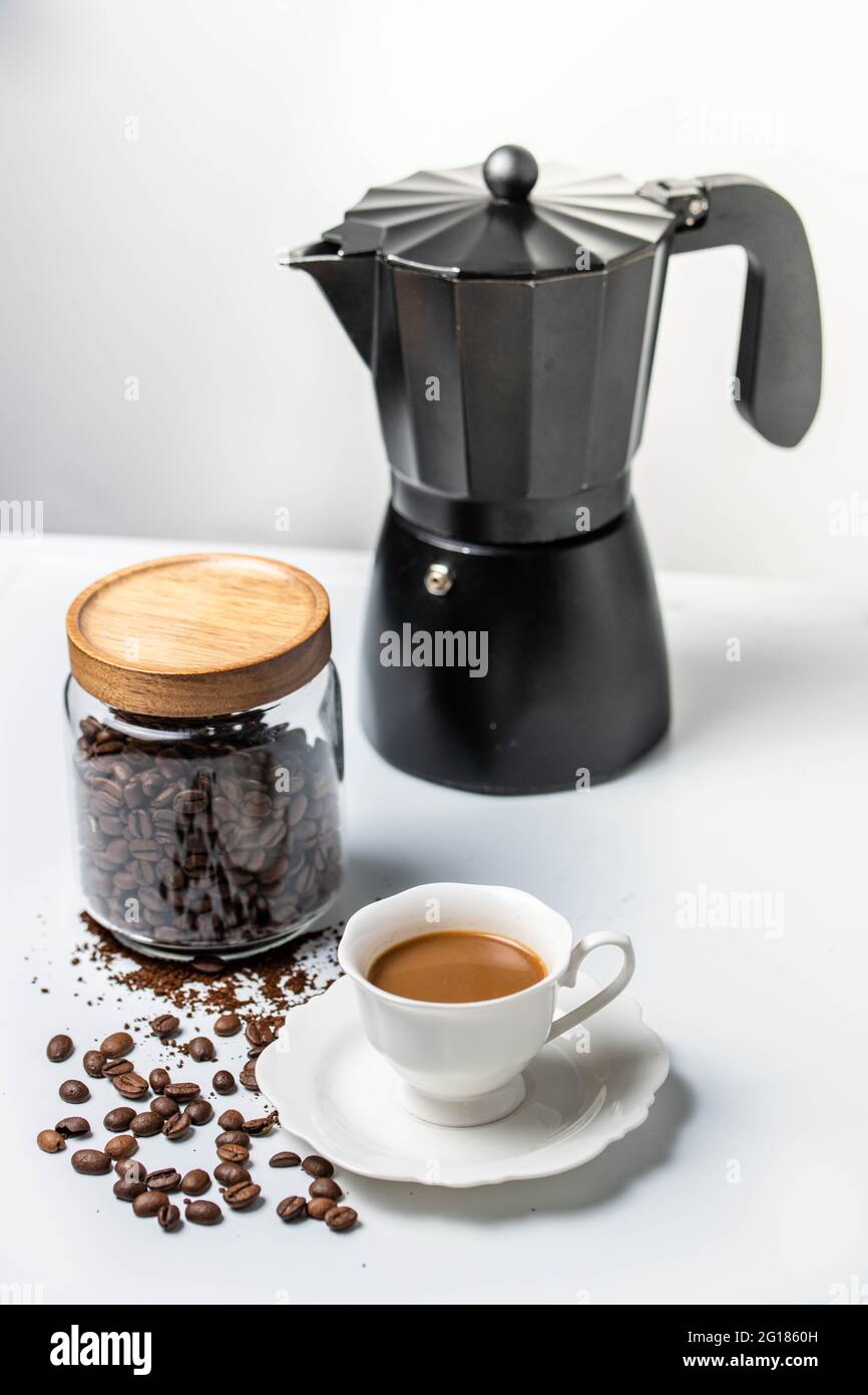 https://c8.alamy.com/comp/2G1860H/little-cute-white-one-china-cup-with-milk-and-coffee-on-a-table-with-black-coffee-maker-and-spread-coffee-beans-2G1860H.jpg
