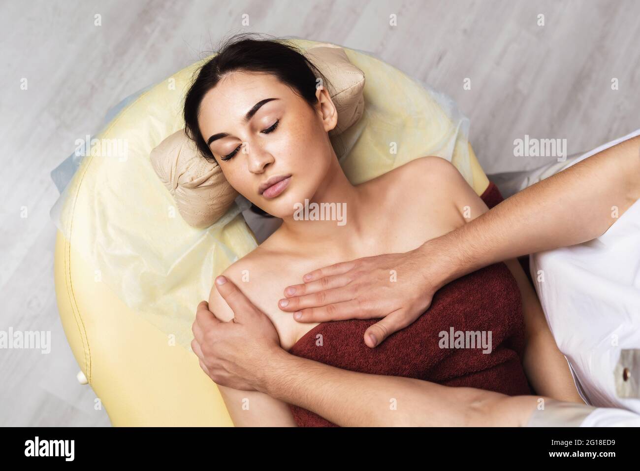 Young beautiful woman is resting during a massage procedure in the area of the collarbone in the spa salon. Stock Photo