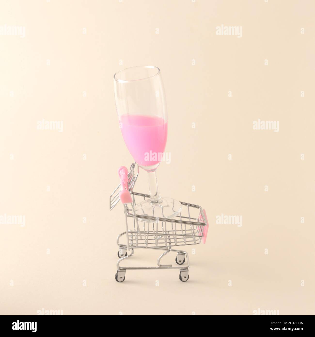 Neon pink champagne drink in a champagne glass set in a shopping cart on a cream background. Summer party concept of shopping and relaxation. Stock Photo