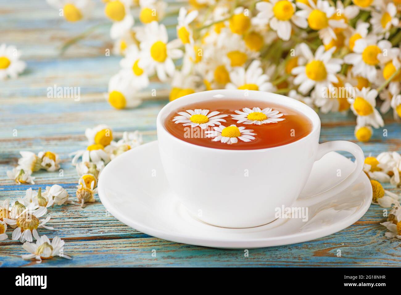 Daisy flowers in a white cup of tea, chamomile herbs on wooden
