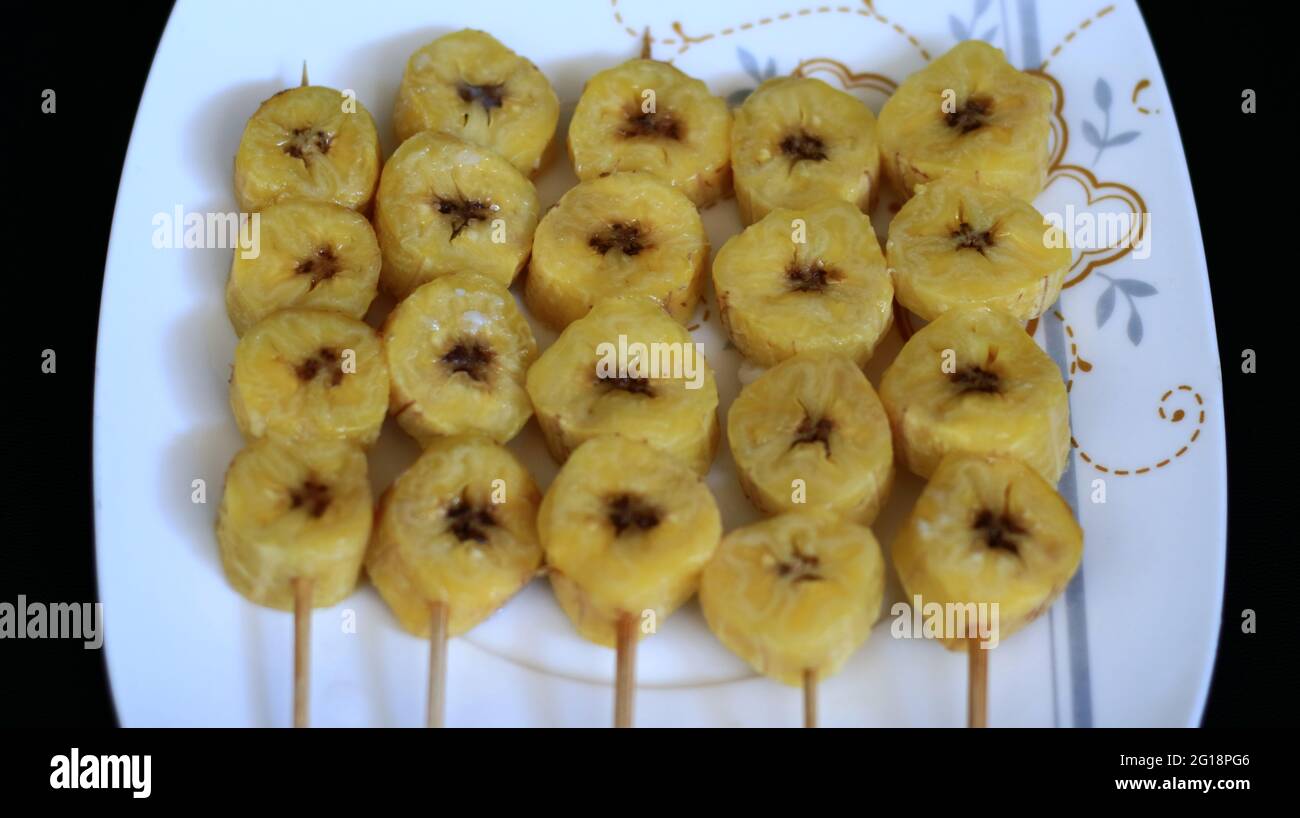 Banana satay on white plate, black background. Stock Photo