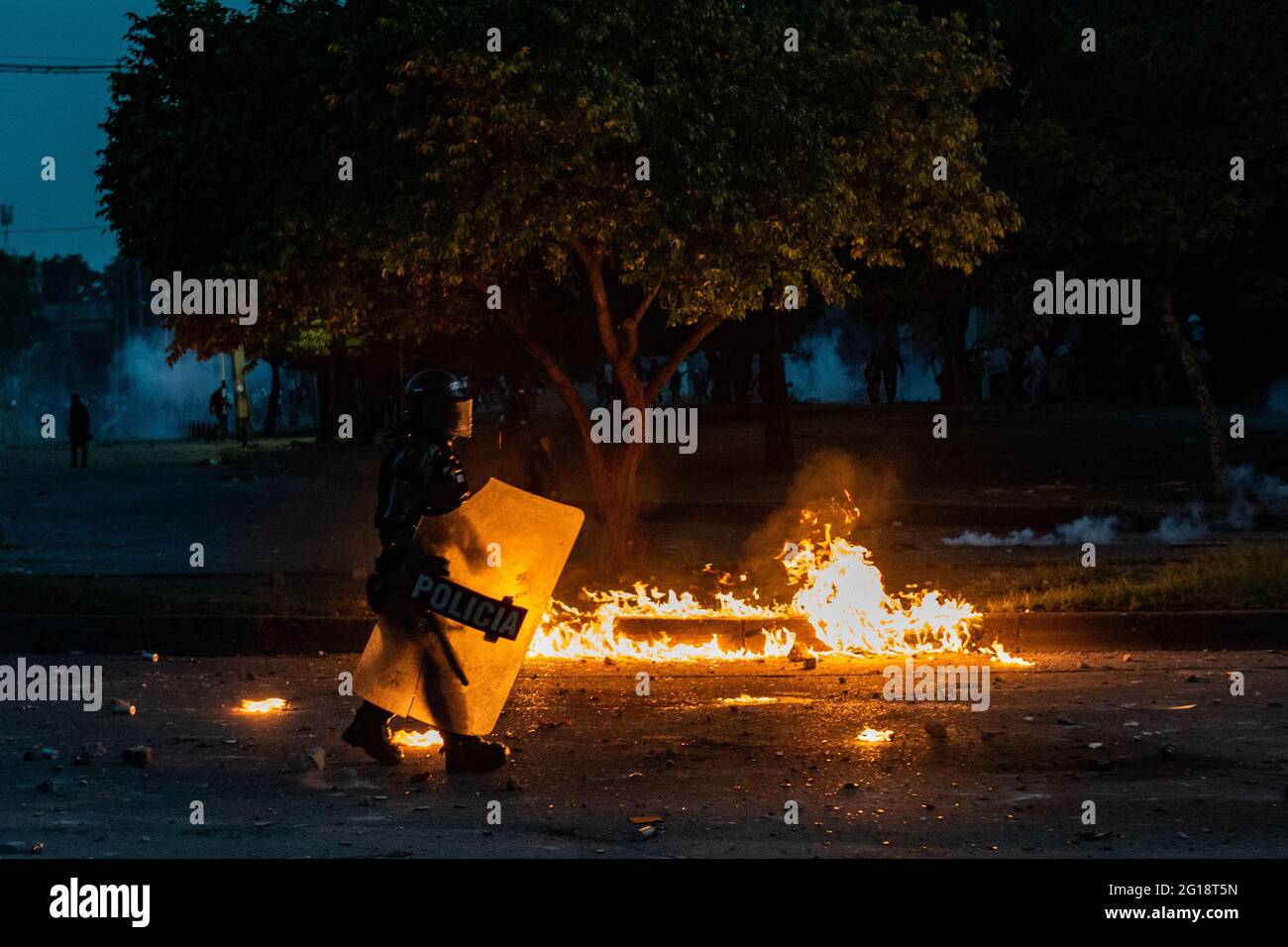 A Colombian riot police officer (ESMAD) walks past a fire as clashes between demonstrators and Colombia's riot police (ESMAD) erupt in Medellín, Colombia after several weeks of anti-government protest against President Ivan Duque's tax and health reforms and unrest and abuse of authority cases that leave at least 70 dead according to NGOs on June 4, 2021. Stock Photo