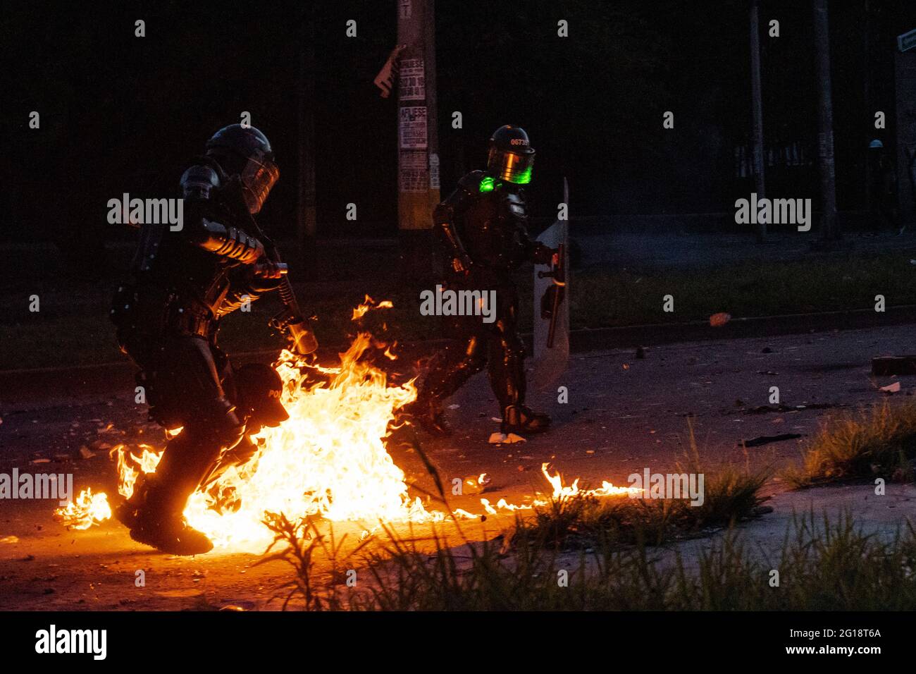 A riot police officer of Colombia (ESMAD) jumps from a molotov bomb that just exploded on its feet as clashes between demonstrators and Colombia's riot police (ESMAD) erupt in Medellín, Colombia after several weeks of anti-government protest against President Ivan Duque's tax and health reforms and unrest and abuse of authority cases that leave at least 70 dead according to NGOs on June 4, 2021. Stock Photo