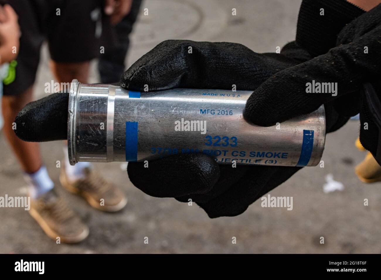 A demonstrator holds a CS tear gas canister with manufacturing date of 2016 as clashes between demonstrators and Colombia's riot police (ESMAD) erupt in Medellín, Colombia after several weeks of anti-government protest against President Ivan Duque's tax and health reforms and unrest and abuse of authority cases that leave at least 70 dead according to NGOs on June 4, 2021. Stock Photo
