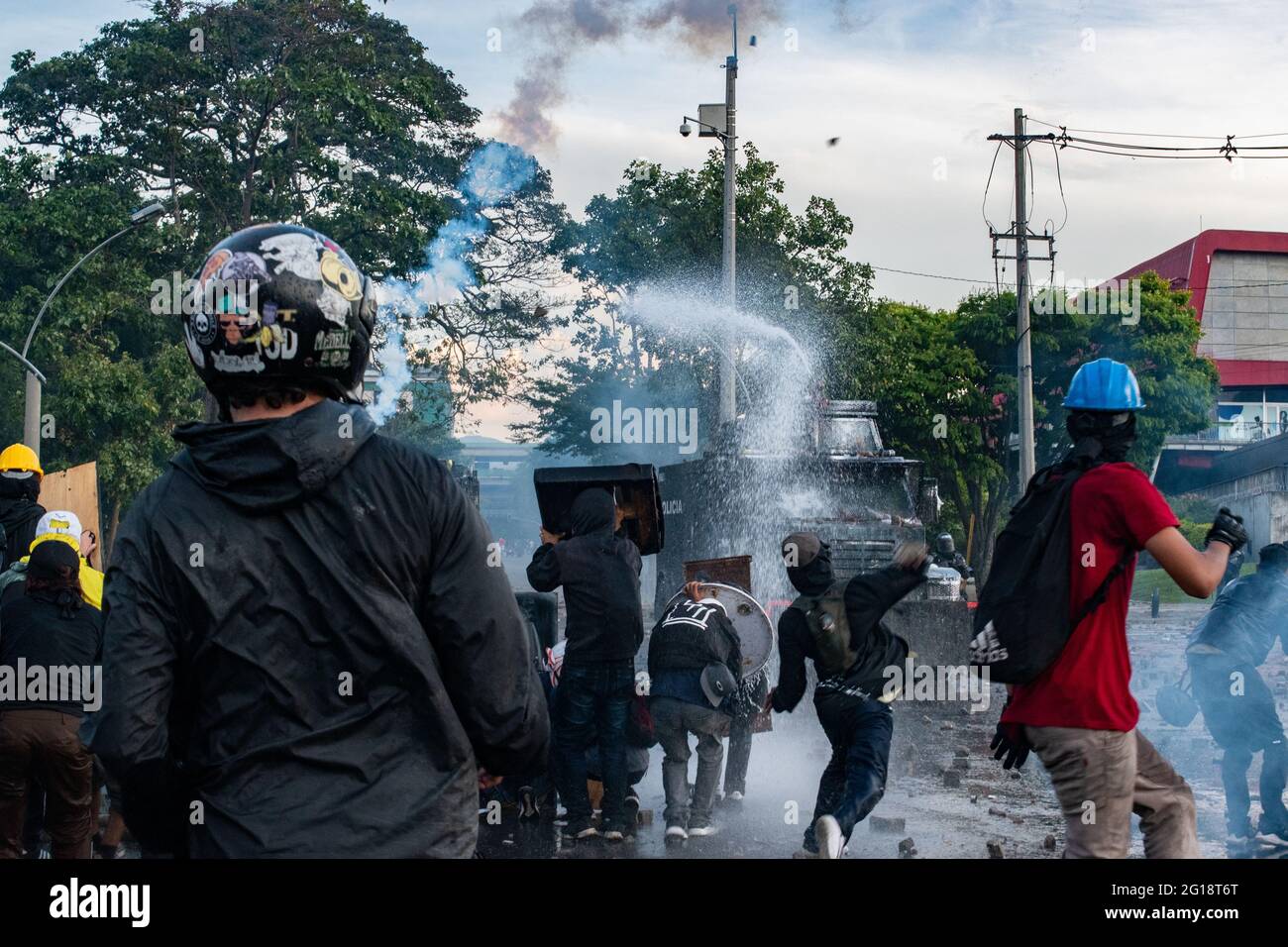 A member of the front line retuns a tear gas canister to a riot armored truck from Colombia's riot police (ESMAD) while it shoots water to demonstrators as clashes between demonstrators and Colombia's riot police (ESMAD) erupt in Medellín, Colombia after several weeks of anti-government protest against President Ivan Duque's tax and health reforms and unrest and abuse of authority cases that leave at least 70 dead according to NGOs on June 4, 2021. Stock Photo