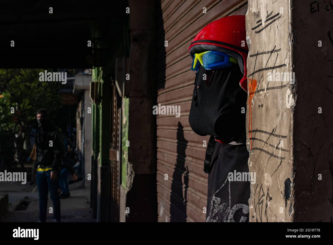 A demonstrator takes cover behind a wall as clashes between demonstrators and Colombia's riot police (ESMAD) erupt in Medellín, Colombia after several weeks of anti-government protest against President Ivan Duque's tax and health reforms and unrest and abuse of authority cases that leave at least 70 dead according to NGOs on June 4, 2021. Stock Photo