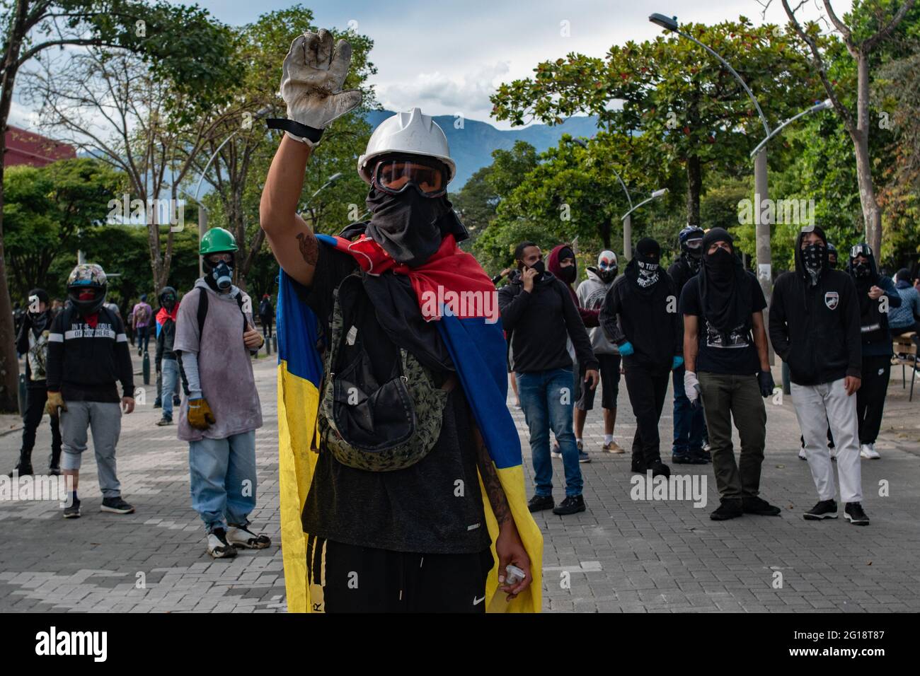 A demonstrator from the front line holds its hand up as he has a Colombia's national flag wrapped on his neck as clashes between demonstrators and Colombia's riot police (ESMAD) erupt in Medellín, Colombia after several weeks of anti-government protest against President Ivan Duque's tax and health reforms and unrest and abuse of authority cases that leave at least 70 dead according to NGOs on June 4, 2021. Stock Photo