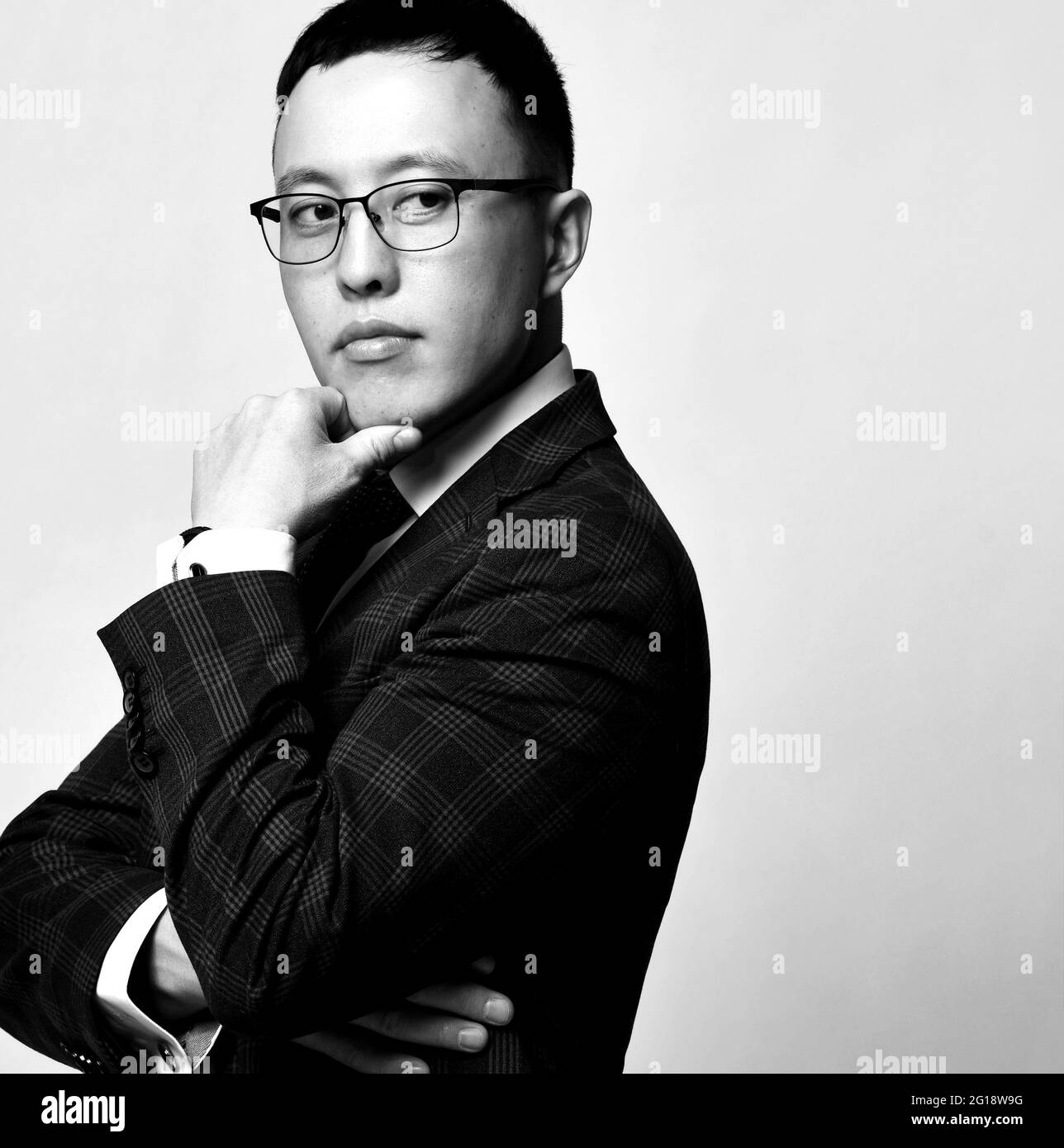 Young businessman in checkered official suit, tie and glasses standing touching chin and looking away Stock Photo