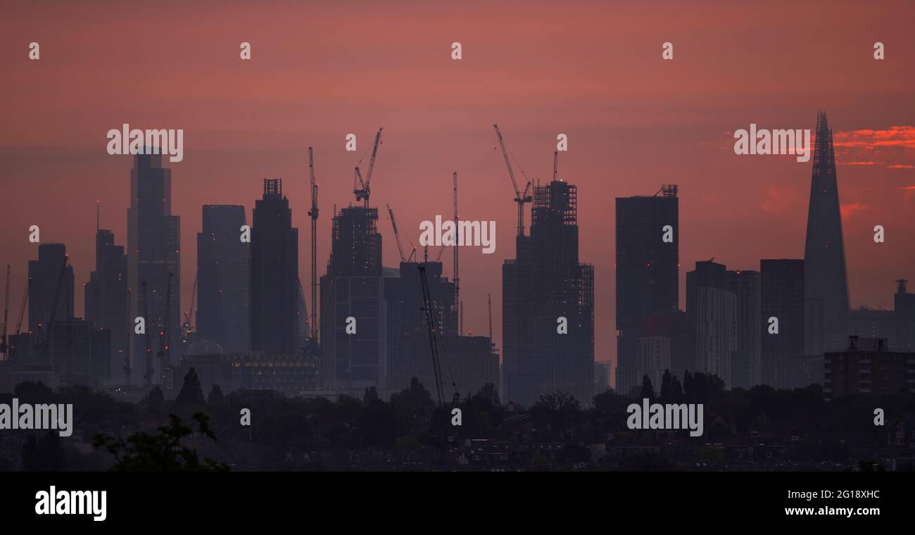 Wimbledon, London, UK. 6 June 2021. Skyscrapers in the centre of London silhouetted against an orange dawn sky. Credit: Malcolm Park/Alamy Live News Stock Photo