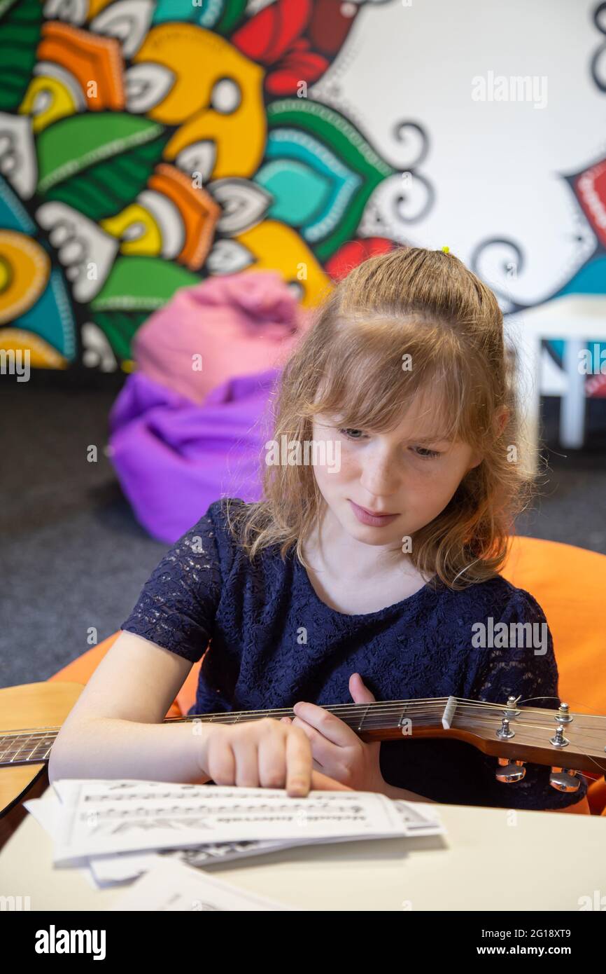 A little girl with a guitar learns solfeggio, sheet music and music theory. Stock Photo