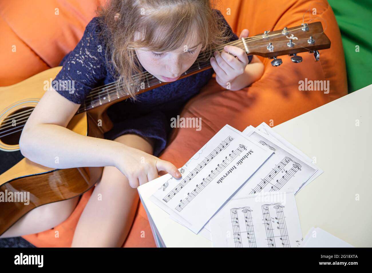A little girl with a guitar learns solfeggio, sheet music and music theory. Stock Photo
