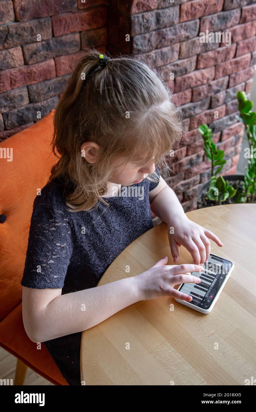 A little girl learns notes in a playful way, with the help of a piano on her phone. Stock Photo