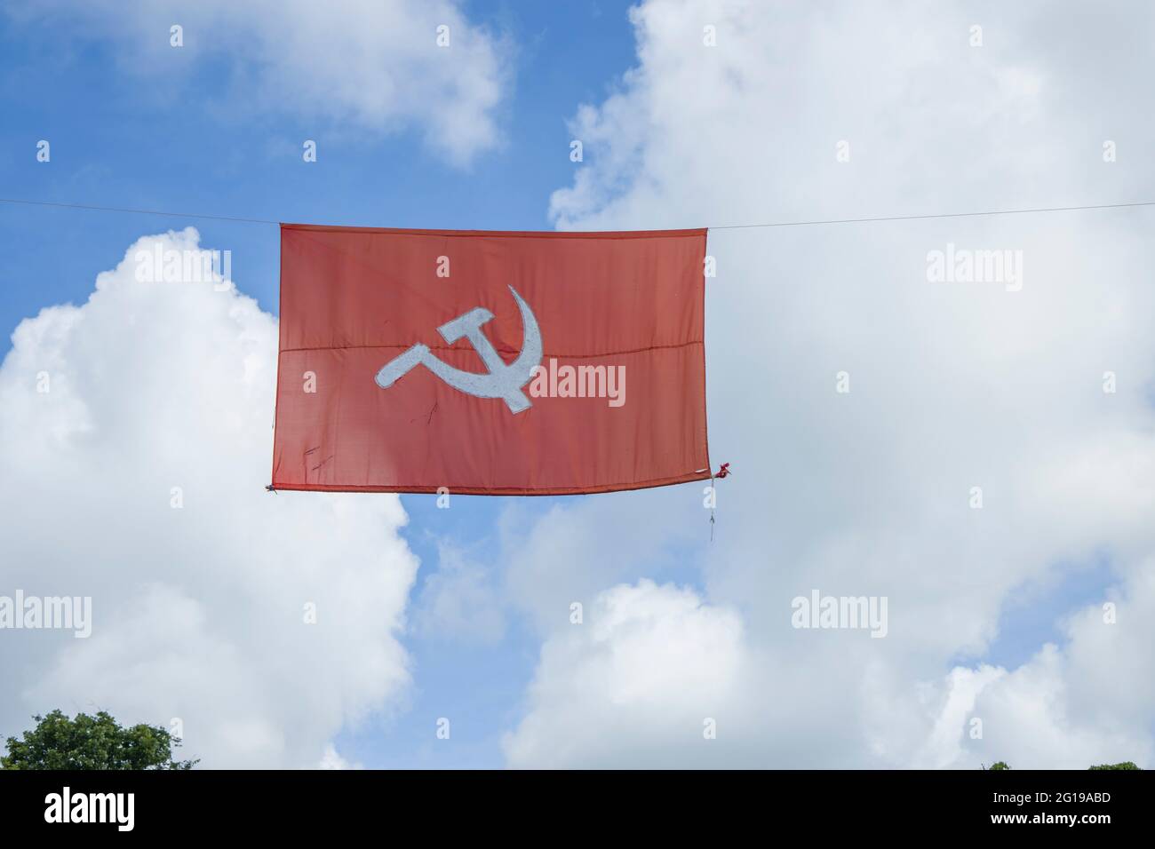 communist flag. Hammer and sickle representing the peasants and the workers, flying in the thick cloudy blue sky. Stock Photo