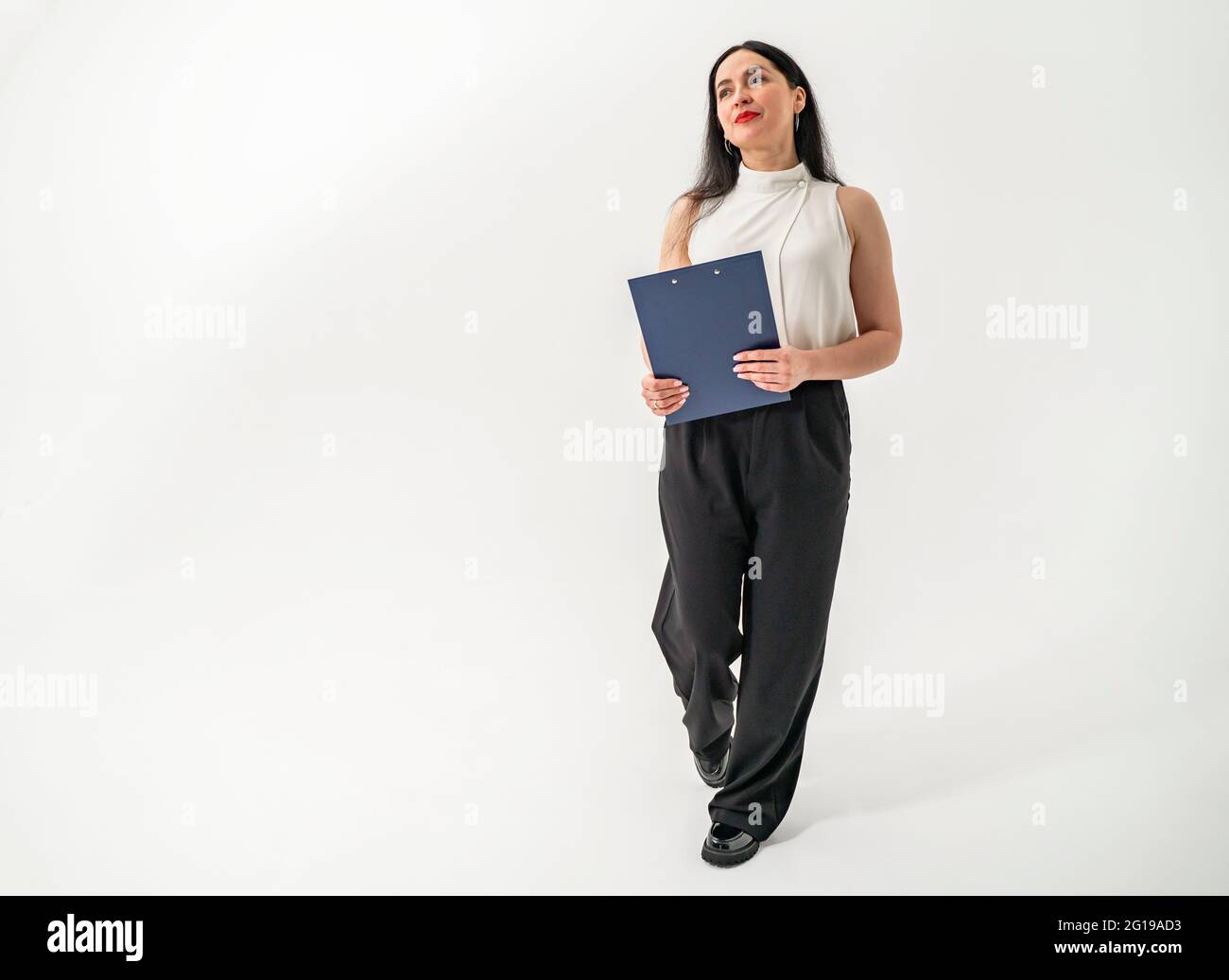 Thoughtful businesswoman holding documents while standing with copy space. Dark-haired student of the higher economic university. Stock Photo