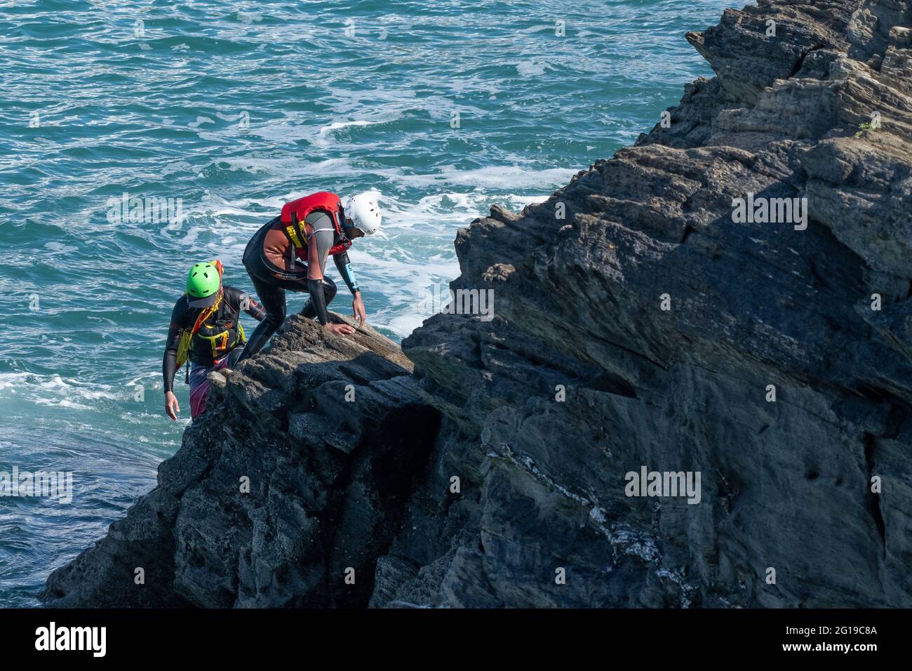 A holidaymaker climbing rocks with a coasteering guide on Towan Head in Newquay in Cornwall. Stock Photo