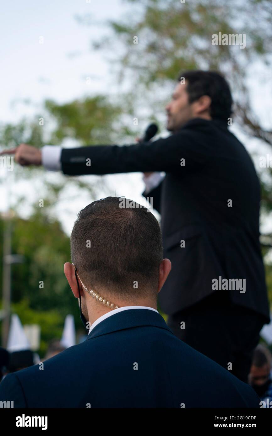 Bodyguard with communications earpiece looking over a politician as he speaks Stock Photo