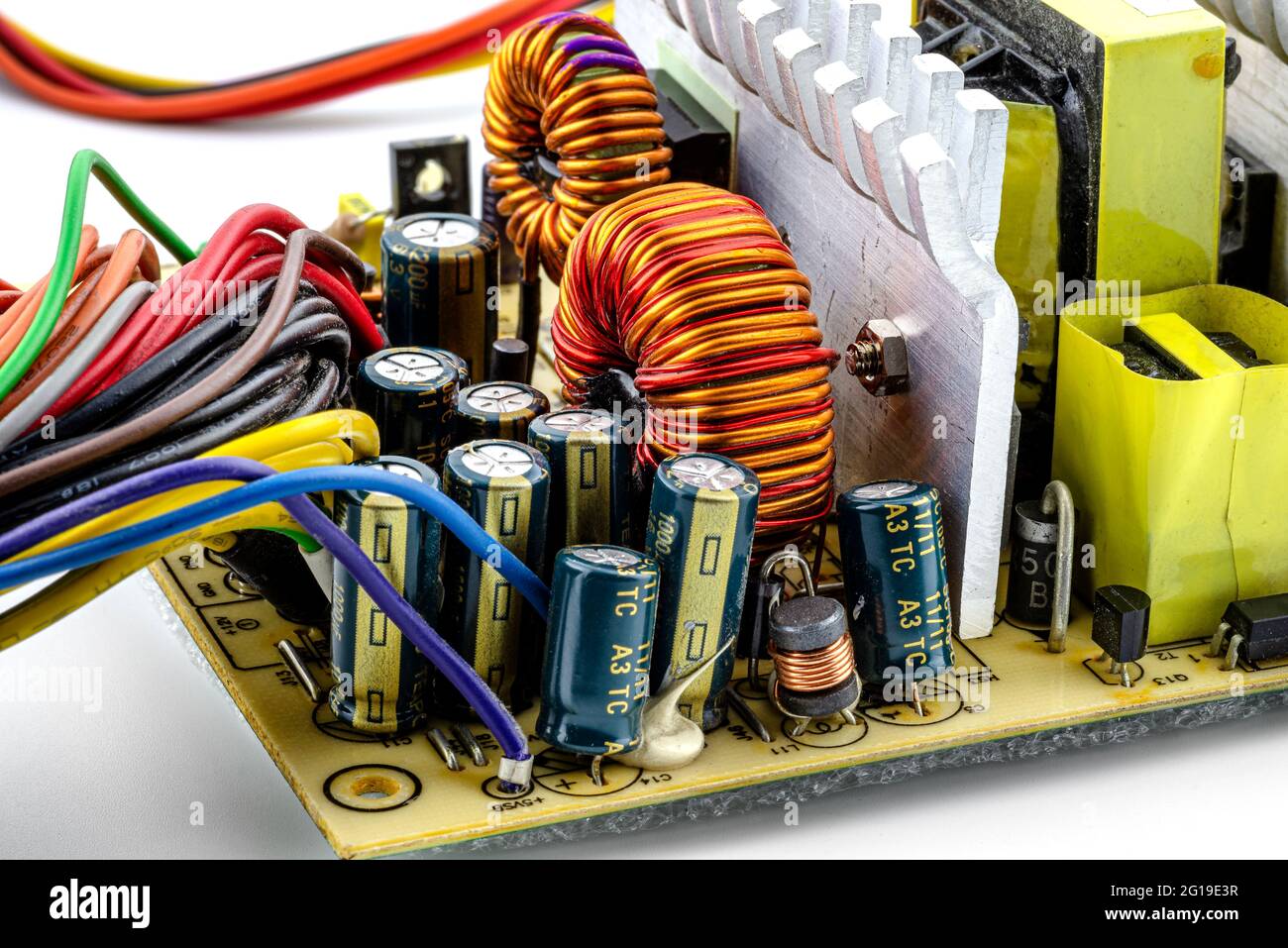 Induction coil, toroidal coil on a ring with visible copper helix and capacitors, mounted on a printed circuit board in a computer power supply. Stock Photo