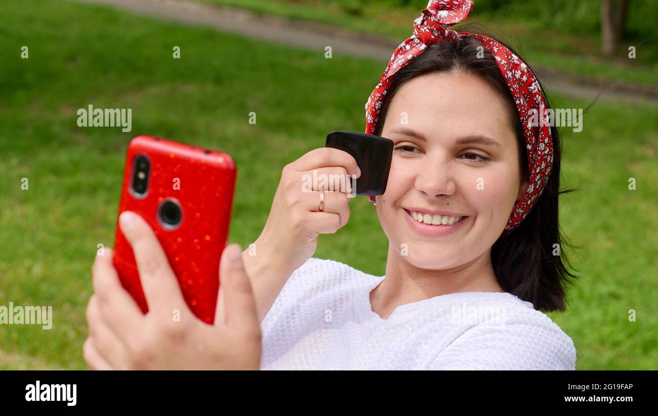 Brunette smiling woman 30 years old, clean fresh face with long hair doing facial massage with gouache scraper outside in front of the phone Stock Photo