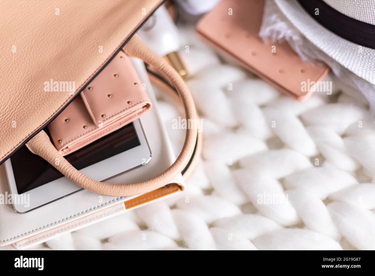 Top view composition organization storage of female handbag lying on white knitted plaid close up Stock Photo
