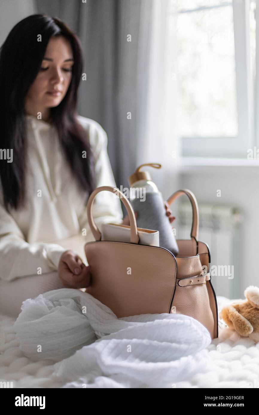 Closeup female hands putting reusable water bottle into handbag getting ready before leaving Stock Photo