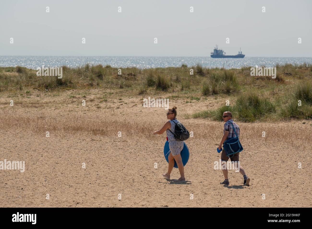 Holiday makers walking on the sand towards the sea with bags in the sunshine heat haze Stock Photo