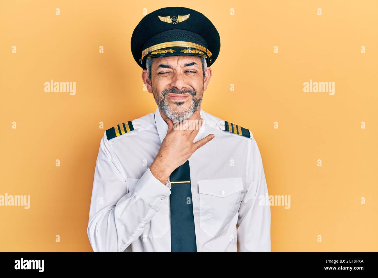 Handsome middle age man with grey hair wearing airplane pilot uniform touching painful neck