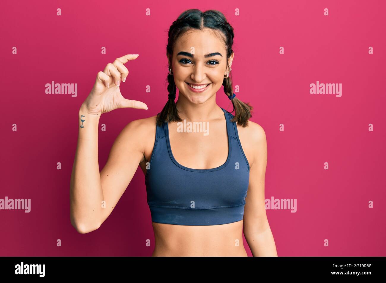 https://c8.alamy.com/comp/2G19R8F/young-brunette-girl-wearing-sportswear-and-braids-smiling-and-confident-gesturing-with-hand-doing-small-size-sign-with-fingers-looking-and-the-camera-2G19R8F.jpg