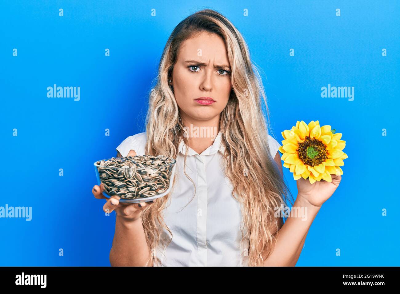 Beautiful young blonde woman holding sunflower seeds an flower skeptic