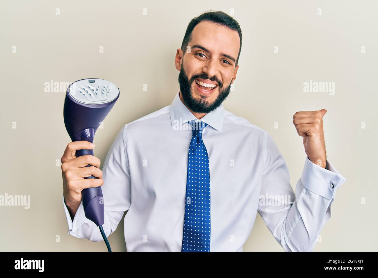 Young business man with beard holding electric steam iron pointing ...