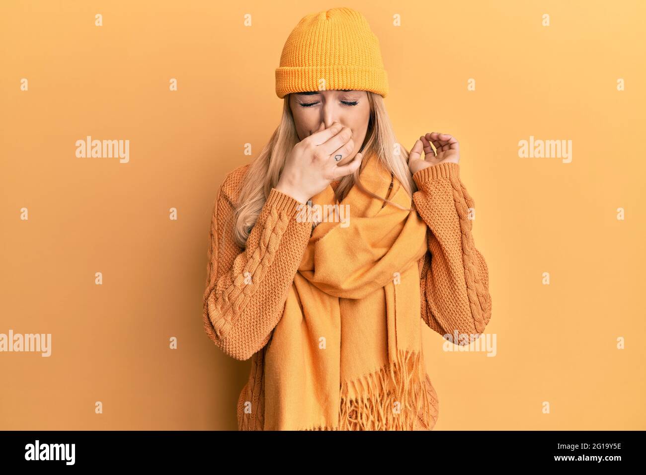 Young caucasian woman wearing wool winter sweater and cap smelling